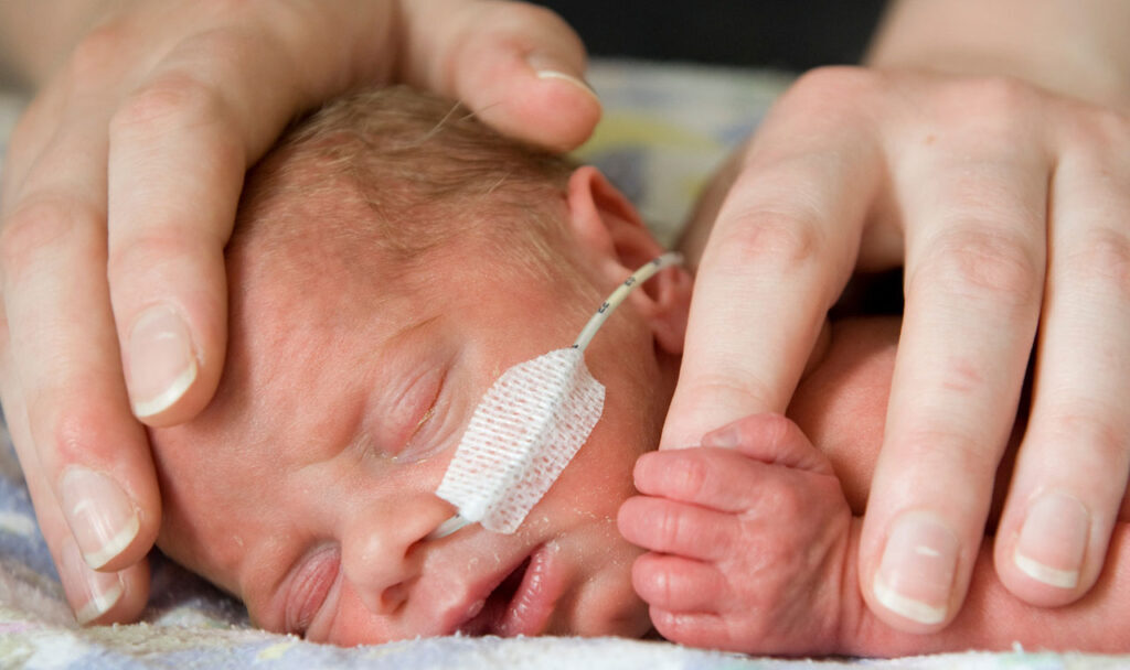 a newborn baby's face with an adults hands next to them