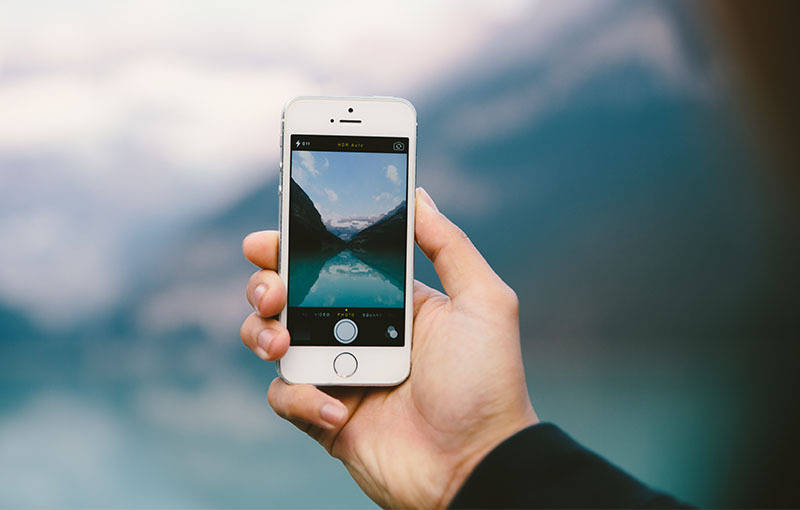 smart phone being held in a hand having just taken a photo of a lake in the mountains