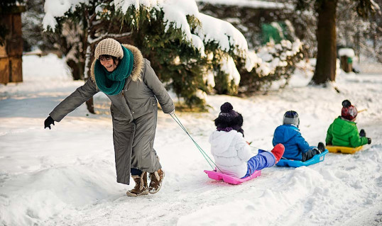 women pulling 3 children on sledges through snow