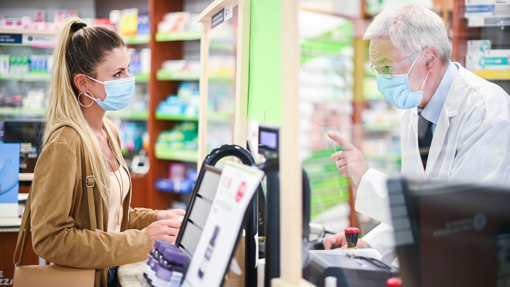 Senior pharmacist dealing with a customer, both of them wearing masks due to coronavirus